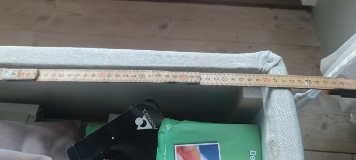 Tumstock som mäter 70 cm längs kanten av en möbel, med tyg och diverse föremål i närheten.