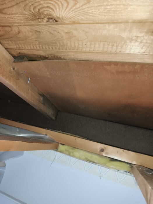 Till synes takbjälkar och isolering, delvis borttagen, med synlig trä- och plastfoliesektion, för renovering av tak och luftspalt.