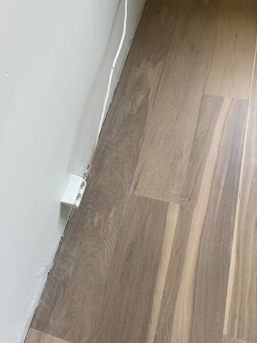 Nyslipat ekgolv med synliga sliprosor och flammighet nära väggen, eluttag på väggen.