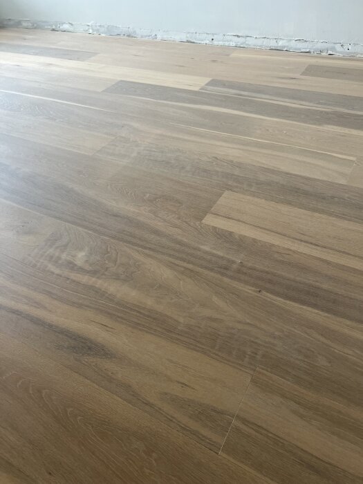 Slipat ekgolv med flammiga områden och små repor, synliga nära en vägg med slitage. Diskussion kring golvslipningens kvalitet.