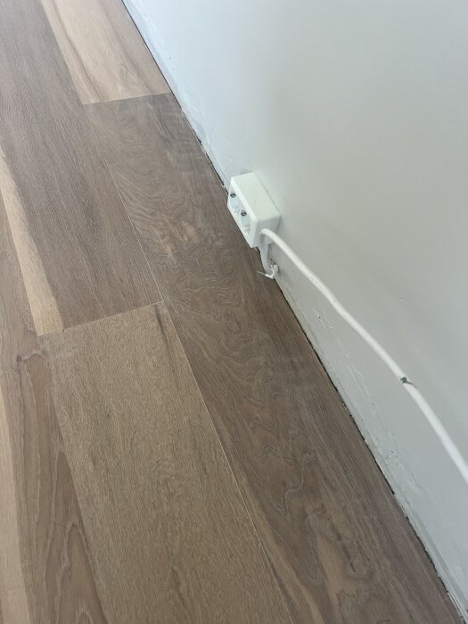 Slipat ekgolv nära vägg med små repor och flammighet; vita elektriska uttag syns.