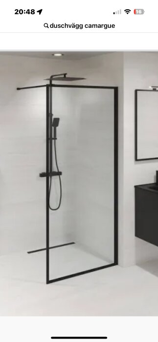 Duschvägg i glas med svart ram, installerad i ett modernt badrum med vita kakelväggar och ett klinkergolv med lutning, duschmunstycke synligt.