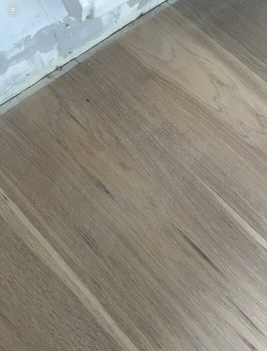 Nyslipat ekgolv med flammiga områden och synliga repor nära en vägg med sliten färg.