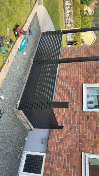 Svart spaljé installerad längs en källartrappa bredvid en tegelvägg, med verktyg och utrustning spridda på marken.