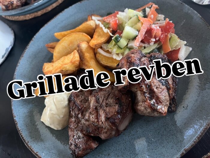 Grillade revben med klyftpotatis, sallad och bea sås på en tallrik.