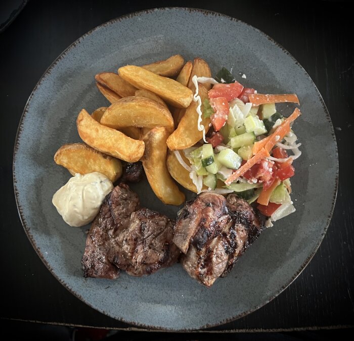 Tallrik med grillade revben, potatisklyftor, sallad och en klick bearnaisesås.