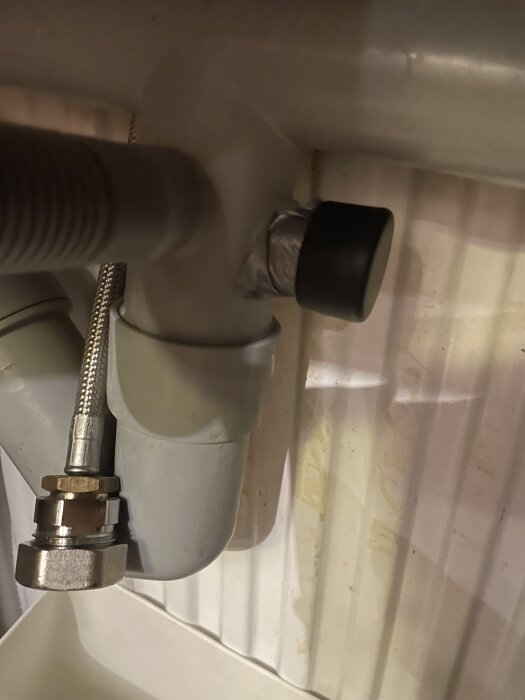 Diskbänkens avloppsrör med en svart propp täckt med silvertejp. Slang och kopplingar synliga.