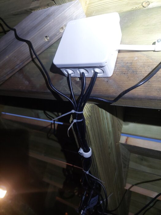 Kablage och en transformator under en trappa, med buntade sladdar fastsatta med klammer och kabelfästen mot trästrukturen.