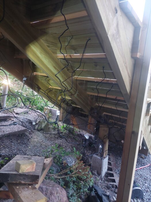Sladdar och träkonstruktion under en trappa, med bundet kablage och spotlights installerade i trappstegen.