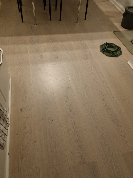 Ljust parkettgolv i ett kök, med ett grönt underlägg bredvid ett av bordets ben.