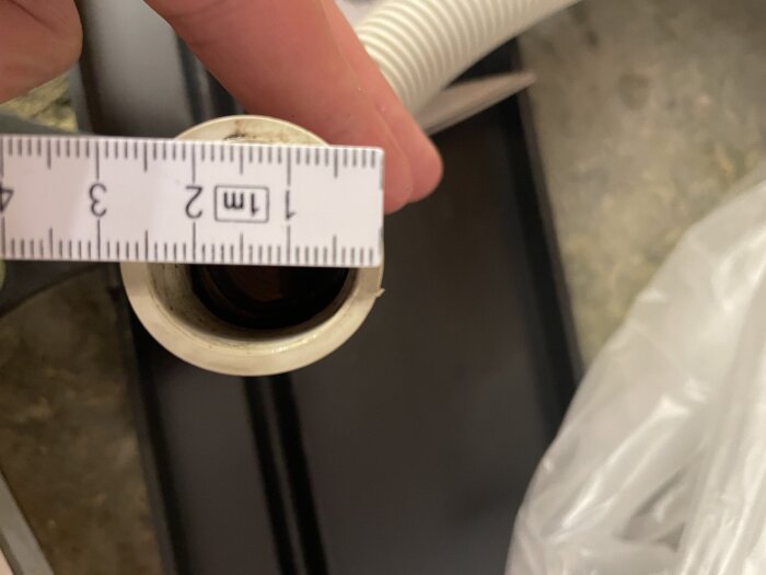 Avloppsslang med en klämma, en linjal visar diameter, mot en suddig bakgrund.