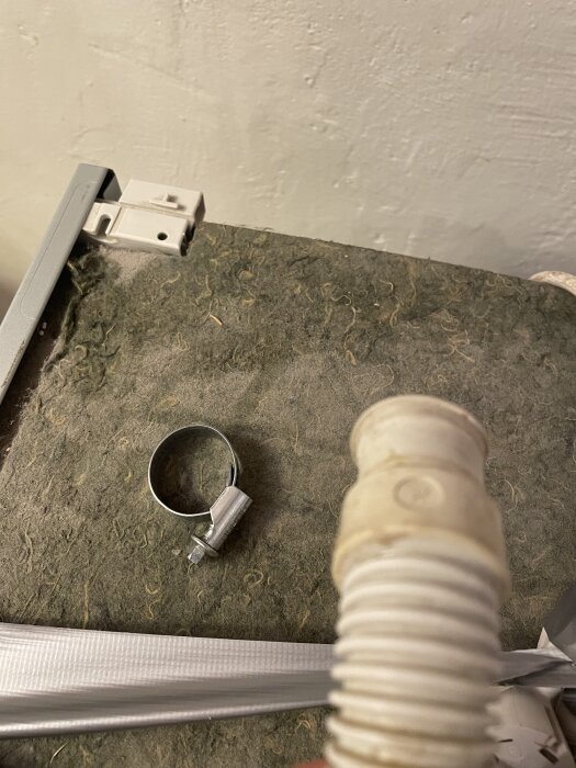 Avloppsslang med metallklämma på texturerat underlag.