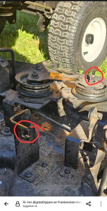 Närbild av en del av en åkgräsklippare med två röda cirklar markerar områden, inklusive vajrar och remskivor nära ett hjul.