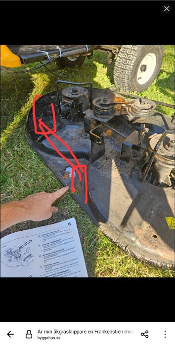 Gräsklipparens klippdäck visas med remskiva och buntband, omgiven av gräs. En hand pekar på däckets del, med textinstruktioner bredvid.