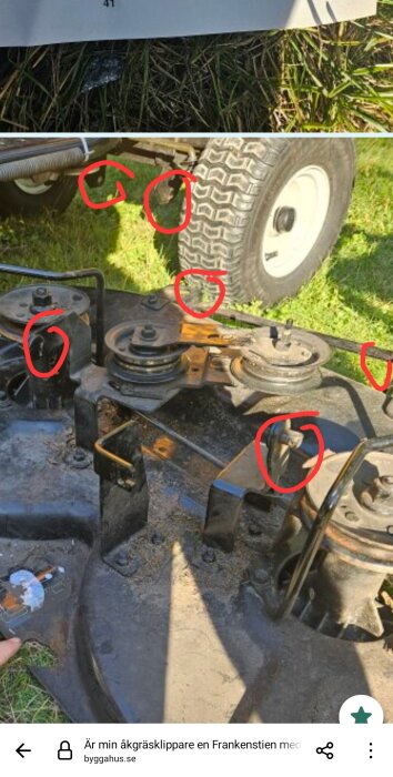 Gräsklippare sedd underifrån med flera röda markeringar runt fästpunkter och hjul på en gräsmatta.