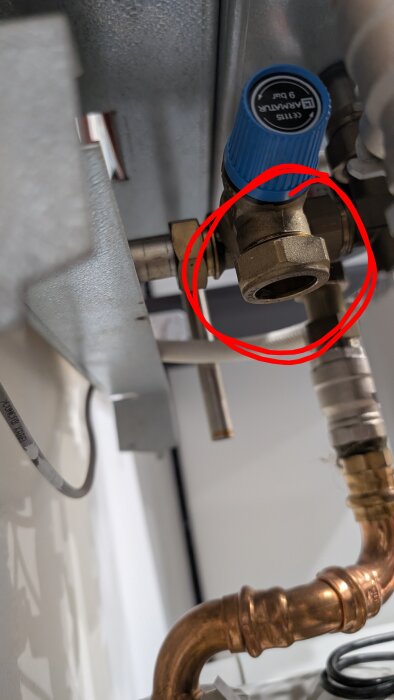 Blåventil i kopparrörsystem, omgiven av rör och anslutningar, del av fjärrvärmesystem, markerad med röd cirkel, potentiellt läckageproblem.