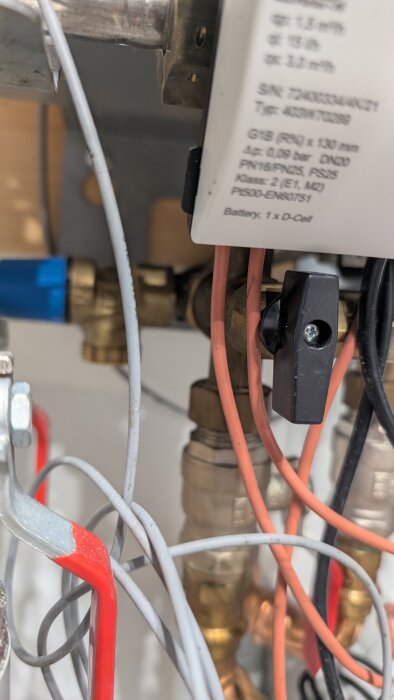 Närbild av en ventil och rörinstallation med elkablar och en komponent med teknisk specifikation på, del av ett rörsystem.