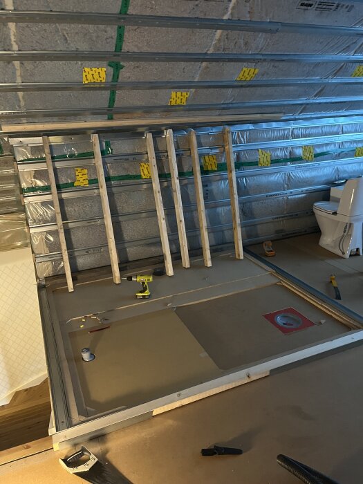 Byggnation av badrum med regelverk och isolering på snedtak, toalettstol i hörnet, verktyg och material utspridda på golvet.