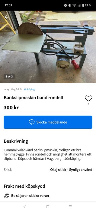 Bänkslipmaskin med band och rondell, placerad i ett garage. Motor och elkablar synliga på golvet. Hemmabyggd maskin till salu för 300 kr.