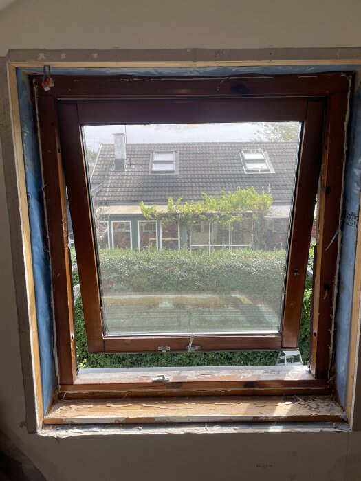 Ett sprucket fönster på övervåningen med utsikt över grannhusets tak. Fönsterkarmen är delvis borttagen för pågående renovering.