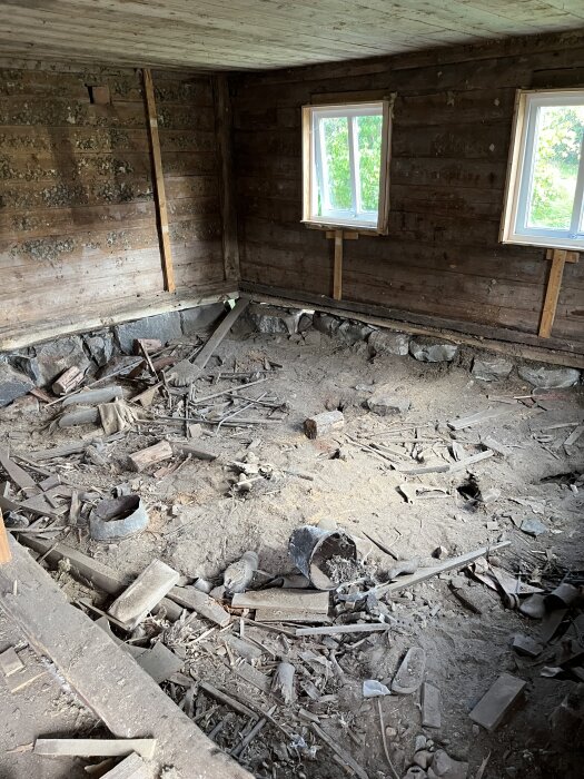 Byggnadens jordiga grund med bråte som träbitar och metallskrot, samt två små fönster som släpper in dagsljus.