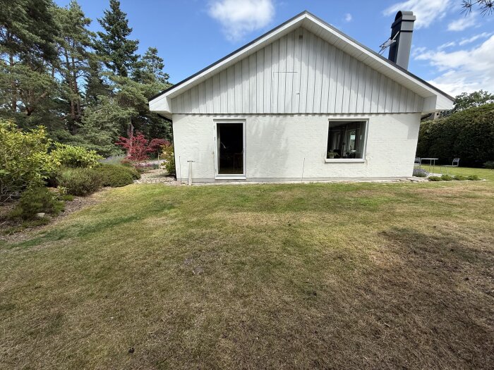 Putsat tegelhus med träpanel på gaveln, omgiven av trädgård och växter. Möjlig plats för planerat orangeri.