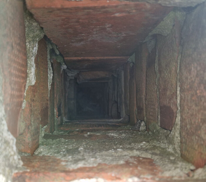 Insidan av en skorstenskanal med tegelväggar, visar en delvis blockerad ventilationsgång i behov av rensning.