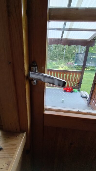 Trästerrass med trasigt fönsterhandtag och utsikt över utemöbler och gräsmatta.