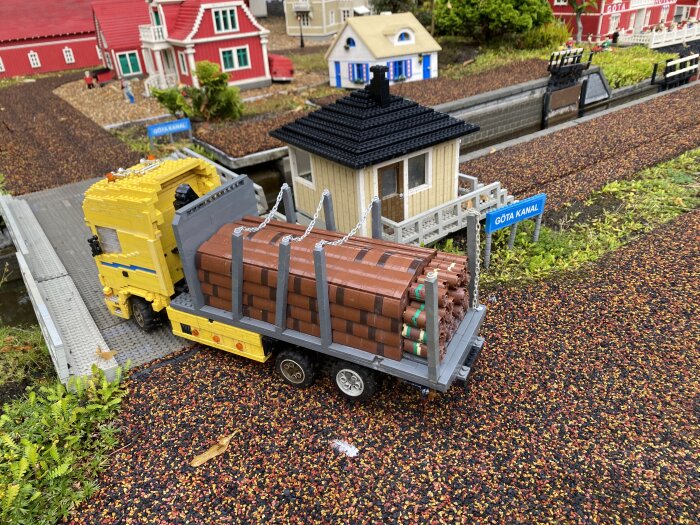 En LEGO-lastbil vid Göta kanal med löst säkrade lastbrädor, byggd av LEGO-delar, omgiven av miniaturbyggnader.
