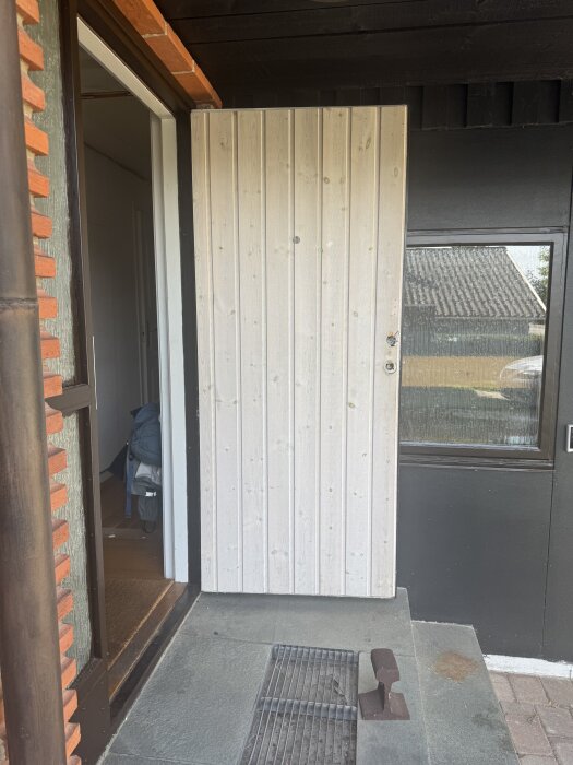 Vita panelplattor applicerade på en ytterdörr med en del paneler i bakgrunden och en dörrmatta på stentrappan.