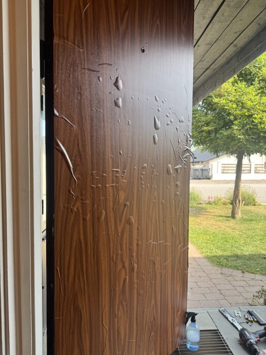 Dekorplast med bubblor och märken på en ytterdörr under renovering, verktyg och en sprejflaska syns vid sidan av dörren.