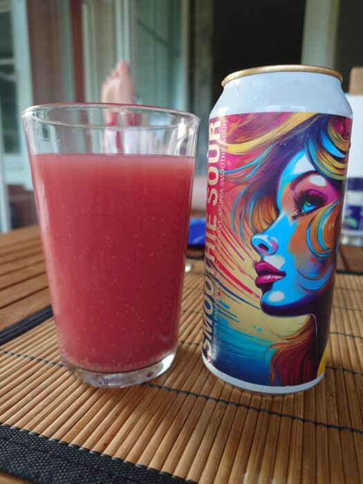 En glas med rosa suröl bredvid en burk med konstnärlig etikett på ett bord.