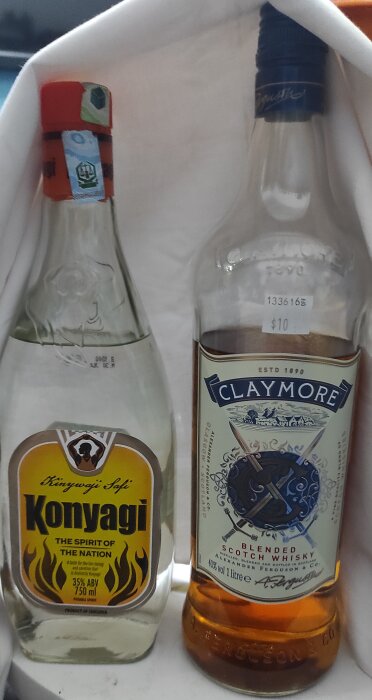 Två flaskor, Konyagi och Claymore Scotch whisky, står bredvid varandra. Prislapparna syns tydligt.