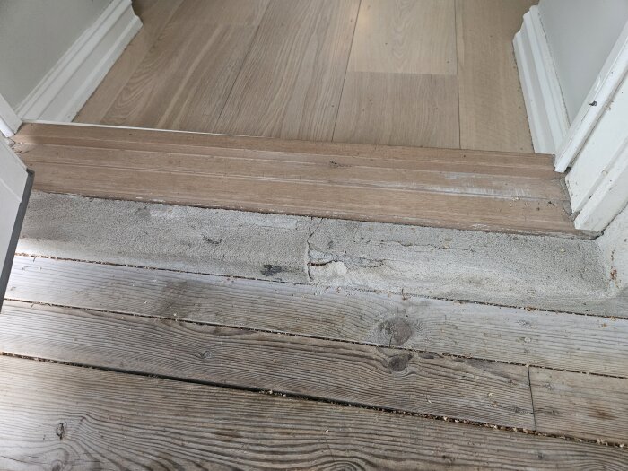 Oskyddad och sliten tröskel vid terrassutgång med murputs som smular ner, övergång mellan trä- och betongyta.