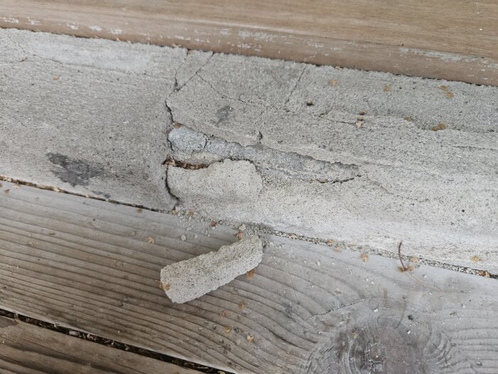 Sprucken och sönderfallande murputs på tröskel vid terrassens utgång, med smulor och bitar som ligger löst på trägolvet.