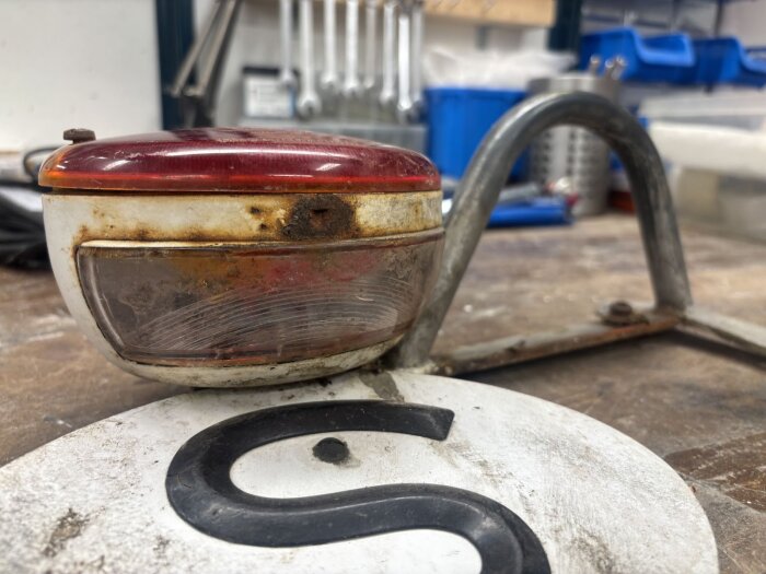 Rostig baklykta på arbetsbänk med S-skylt i metall.