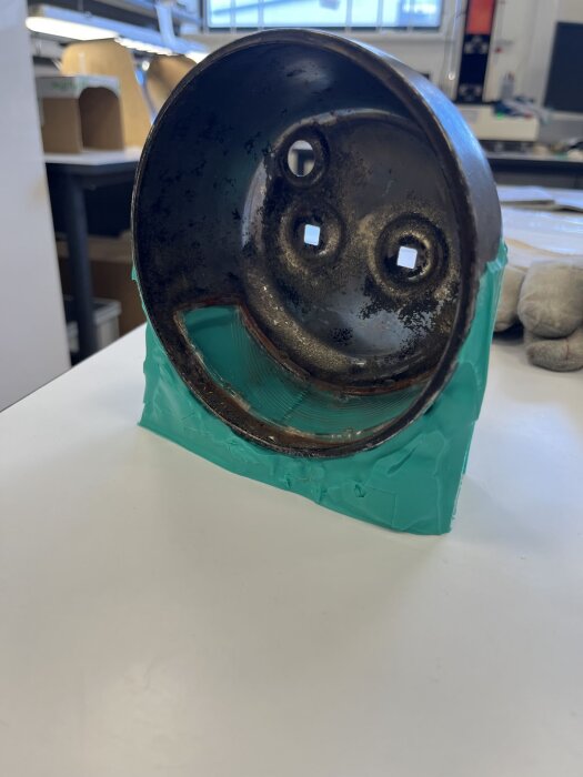 Gammal, rostig baklykta med turkos silikonform för renovering, stående på ett vitt bord i en verkstadsmiljö.