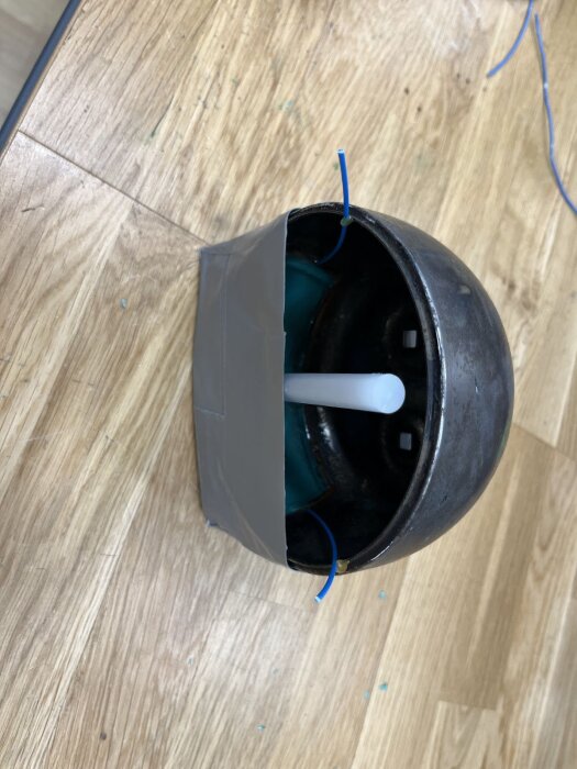 Rund lykta med silverfärgad tejp och blå tråd monterad på undersidan, står på ett ljust träbord.