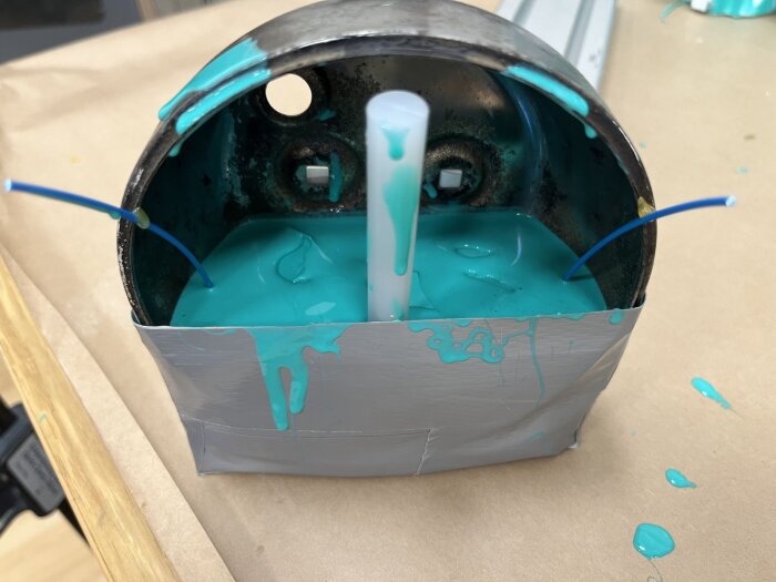 Gammal baklykta omgiven av tejp och fylld med turkos silikon för formgjutning, två blå kablar och en vit stav sticker upp från formen.