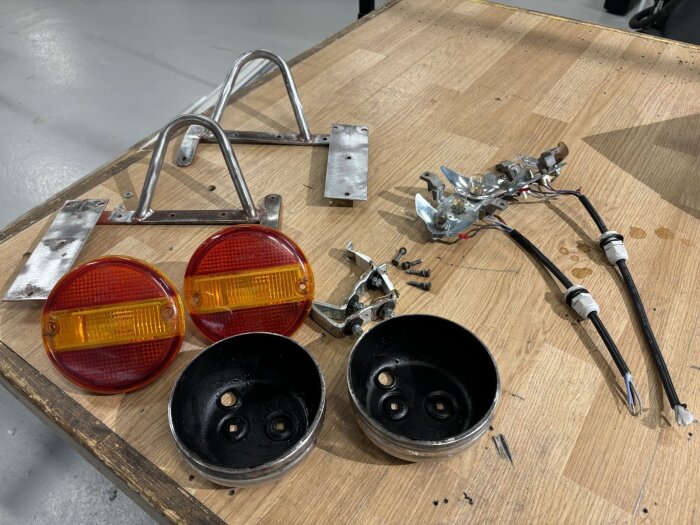 Gammal billykta i delar på ett bord, inklusive två runda röda och gula glas, metallfästen, skruvar och kablar redo för renovering och montering.