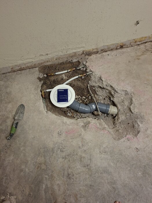 Renoverad tvättstuga med nytt avlopp och golvbrunn, omgivande mark och ett verktyg synligt på betonggolvet.