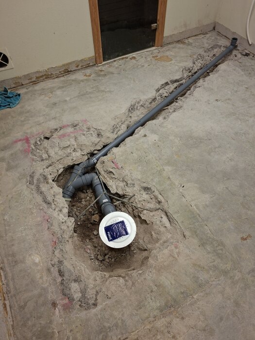 Renoverad tvättstuga med nytt avloppsrör och golvbrunn, omgiven av uppbruten betong, med en renslucka synlig i golvet.