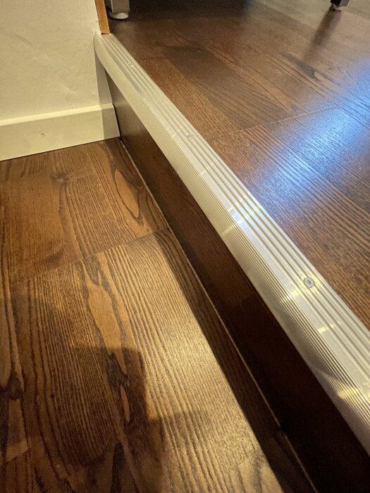 Trägolv med monterad kvartslist i hörn, fokus på skarv mot vägg.