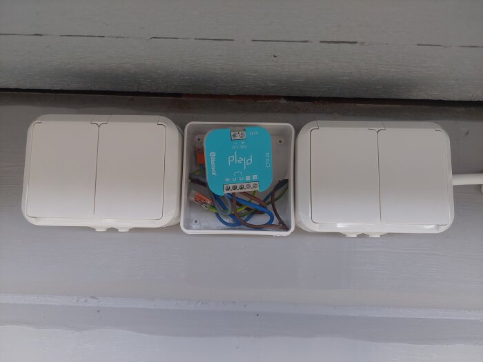 Elinstallation med Plejd-enhet monterad i en dosa på vägg för styrning av ljusslinga, med synliga kablar och två strömbrytare bredvid.