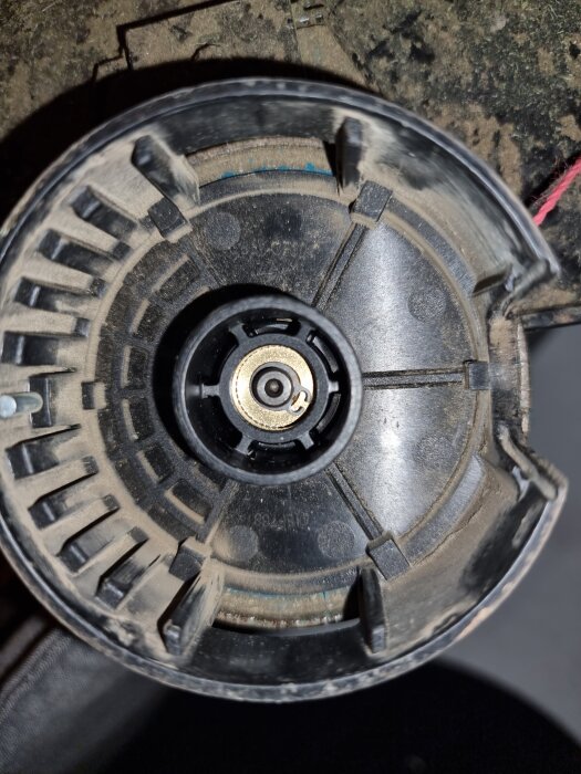 Närbild på en grästrimmerdel med fastnat snöre, centralt syns en låsring.