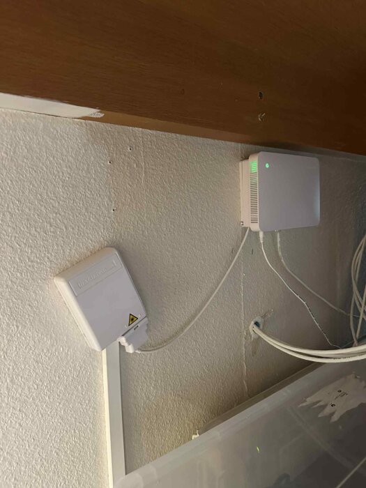 Två väggmonterade vita boxar med kablar anslutna; den mindre är snedställd medan den större har gröna ljusindikatorer.