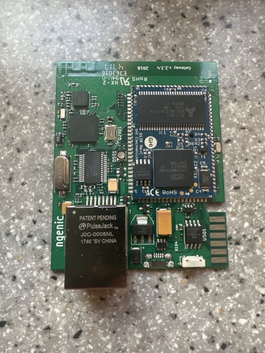 Äldre modell av gatewaykretskort med exponerad hårdvara, inklusive IC-chips och nätverksport, ligger på en mönstrad yta.