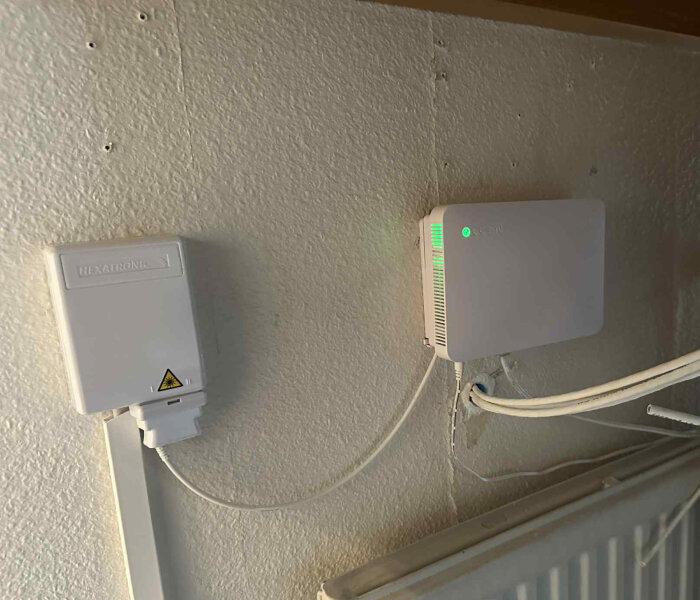 Väggmonterad elektronisk enhet bredvid en Hexatronic anslutningsbox, med gröna lampor som indikerar funktion.