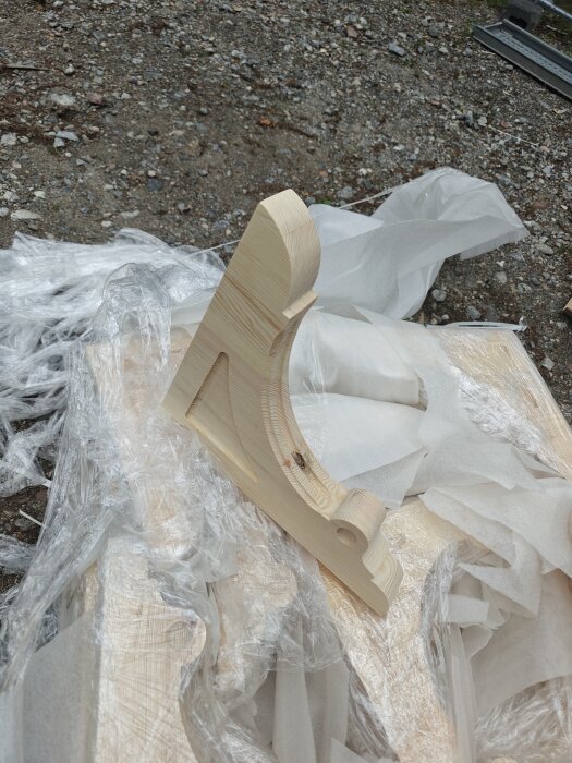 Träkonsol prototyp liggande på marken, omgiven av plast och packningsmaterial.