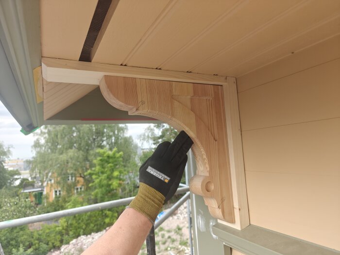 Hand i handske installerar träkonsol under takfot på husfasad.